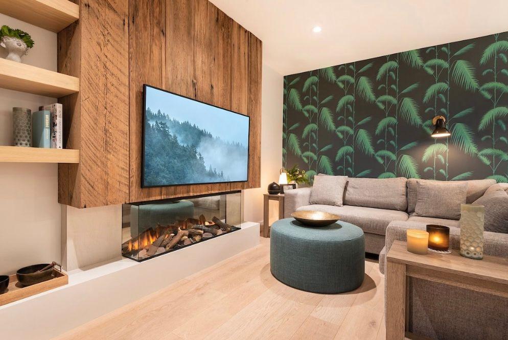 Modern living room with a wooden wall, fireplace, large sofa, and tropical-themed wallpaper.