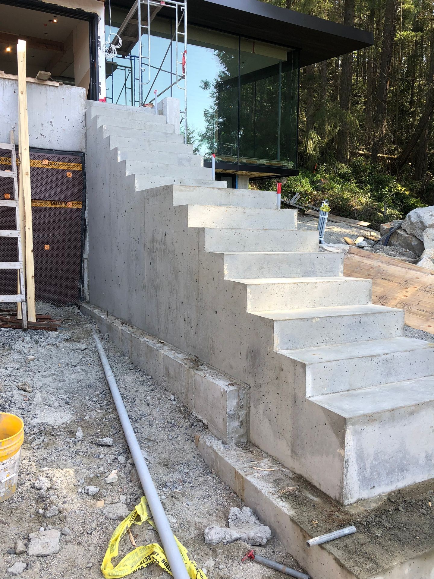 Concrete stairs under construction leading up to a building with glass walls, surrounded by construction materials.