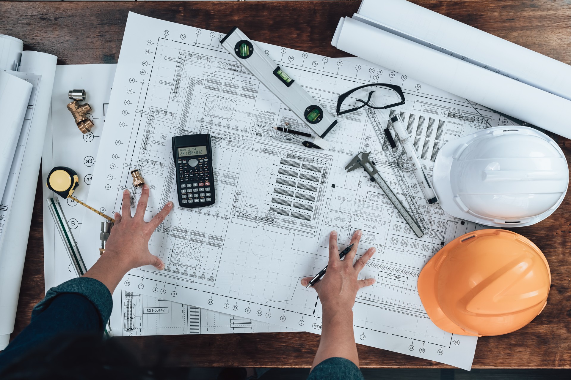 Top view Engineering working with drawings inspection and press calculator on the office desk and triangle ruler, safety glasses, compass, vernier caliper on Blueprint. Engineer, Architect, Industry and factory concept.